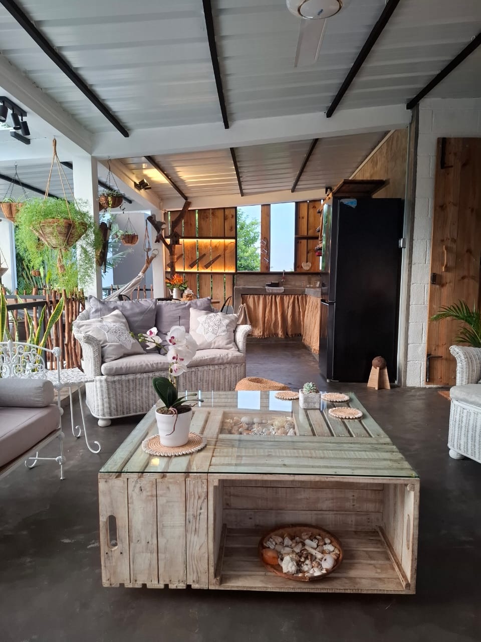 Le grand espace commun ouvert sur le jardin, canapés en rotin et cuisine au fond